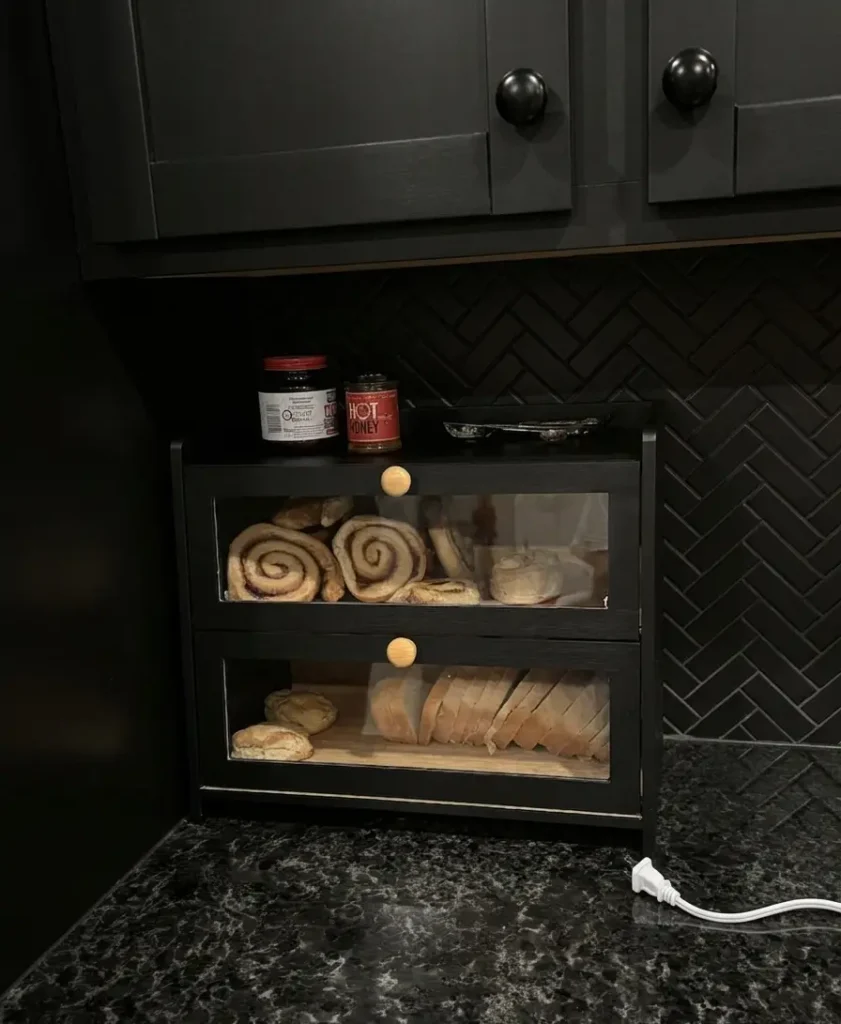 JANSNIMEN Bread Box Countertop Farmhouse Review — The 2-Layer Bamboo Storage Upgrade Your Kitchen Actually Needs
By Norman | Alidealshub.com | Kitchen Storage & Organization

Quick Key Takeaways

Two separate compartments let you store different baked goods without mixing smells or crumbs
Made from natural bamboo with a sleek matte black finish — looks great in modern and farmhouse kitchens
Strong magnetic closure on both doors keeps bread fresh without fumbling with latches
Clear front windows mean you always know what's inside — no more forgotten loaves going moldy
Top shelf with anti-drop fence doubles as extra counter storage for spices, condiments, or your toaster
Generous size (15.7" × 9.5" × 13") fits full-size loaves, pastry bags, bagels, and more
Versatile enough to store dishes, pantry snacks, and small appliances when used with doors open


Let Me Tell You Something About Bread (And Why It's Always Ending Up Stale)
Let me paint you a picture real quick.
It's 7 AM on a Tuesday. You're rushing to get breakfast going, and somehow your loaf of bread is squashed under a bag of bagels. The muffins from yesterday are sitting naked on the counter. The croissants from Saturday are already stale because — honestly — they were just hanging out in open air doing absolutely nothing. And the counter? A complete mess.
We've all been there.
For the longest time, I just assumed bread storage was one of those unsolvable kitchen problems. You either squeeze everything into a tiny metal tin that doesn't close properly, or you're drowning in plastic bags scattered across the counter. Neither option works well. And honestly? Neither one looks good either.
So when I came across the JANSNIMEN Bread Box Countertop Farmhouse, I was genuinely curious. Two full layers of storage, natural bamboo, a clear window on each compartment, magnetic doors, and a fenced top shelf you can actually use for something else? That's a lot of features packed into one countertop unit.
Here's my full honest take — everything you need to know before you decide if it's right for you.

What Is the JANSNIMEN Bread Box — And Who Is It Really For?
In simple terms, this is a two-tier countertop storage unit made from natural bamboo with a matte black painted finish. It sits right on your kitchen counter and gives you two front-opening compartments — each with a clear acrylic window and a warm wooden round handle — plus a flat top shelf with a raised fence to keep things from sliding off.
Now, you might be thinking, "it's just a bread box." But here's the thing — this product actually solves more than just a bread problem. It's really about reclaiming your countertop and creating a little kitchen station that pulls its weight in multiple ways. If you're someone who loves smart countertop organization, you might also want to check out our guide on Forest Angle Angled Countertop Storage — another great option for keeping your kitchen neat and functional.
This is a great fit for:

Families who go through a full loaf every couple of days and need serious storage space
Home bakers who regularly have multiple types of baked goods sitting out at once
People who want a clean, organized kitchen that actually looks good
Renters or apartment dwellers with limited cabinet space who need smart countertop solutions
Anyone with a farmhouse or modern kitchen aesthetic who doesn't want a plastic bin ruining their vibe

Honestly, even if you're not a big bread person, this box is worth considering purely as a multi-purpose kitchen organizer.

Key Features and What They Actually Mean in Real Life
Here's the part most reviews skip — breaking down not just what a feature is, but what it actually does for you on a regular Tuesday morning.
1. Natural Bamboo Construction
Bamboo is naturally moisture-resistant, which matters a lot when you're storing baked goods. It won't warp or swell the way cheaper fiberboard does over time. The matte black finish also hides everyday smudges and fingerprints way better than lighter-colored materials. This thing will still look good a year from now.
2. Clear Front Windows
This is honestly one of my favorite details on the whole product. Each compartment has a clear acrylic window so you can see what's inside at a glance — without opening anything. No more reaching blindly into a dark box and discovering the bread went bad three days ago. You see it, you remember it, you use it. Simple, but brilliant.
3. Strong Magnetic Closure
Both drop-front doors snap shut with a magnetic closure. There are no clips, latches, or awkward swinging doors to deal with. You just press it closed and the magnet holds it firmly in place. It creates a snug seal that keeps air out, which genuinely helps bread stay fresher longer compared to a loose-fitting container.
4. Large Dual-Layer Capacity
At 15.7 inches wide and 13 inches tall, this is not some dainty decorative box. Each of the two compartments is 5.5 inches tall — wide and deep enough for a full-size sandwich loaf, a stack of bagels, a baguette, or even a box of pastries from your local bakery. Two levels also means different baked goods don't have to share the same space. No mixing, no crumb cross-contamination.
5. Anti-Drop Fence on the Top Shelf
The top surface is flat with a low raised fence on three sides — and that little detail makes a bigger difference than you'd expect. You can set a toaster, jars of jam and peanut butter, a bottle of hot sauce, or condiments up there without worrying about them sliding off the edge. It transforms the top of your bread box into a genuinely useful kitchen shelf. If you're also thinking about other smart ways to use your counter space, our post on Forest Angle Angled Countertop Storage covers some really creative options worth exploring.
6. Waterproof Surface
The bamboo is treated to resist moisture. If you accidentally spill water, honey, or juice on it, you can wipe it clean without staining or damaging the surface. For a kitchen item that's handling food every single day, this is a must-have feature — not just a nice-to-have.
7. High-Foot Bottom
The box sits on elevated feet, which keeps the base off the counter surface. This improves airflow underneath, makes cleaning much easier, and prevents moisture from getting trapped at the bottom over time. A small detail, but thoughtful design always shows up in the small things.

Honest Pros & Cons
No product is perfect, and I'd rather be straight with you than oversell anything.
Pros:

Two separate compartments — genuinely rare at this price range
Looks beautiful on a kitchen counter — guests will notice it
Bamboo is durable, eco-friendly, and built to last
Magnetic closure is satisfying and keeps the seal snug
Clear windows eliminate the "mystery box" problem completely
Fenced top shelf adds real, functional surface space you'll actually use
Waterproof coating is practical for everyday kitchen life
Generous size without being bulky or overwhelming on the counter
Versatile — works for dishes, pantry goods, snacks, and kitchen appliances too

Cons:

Currently only available in black — may not suit very light or all-white kitchens
The clear front panels will show crumbs over time if you don't wipe them down regularly
May feel slightly oversized on a very small counter or in a studio apartment kitchen
Requires a few minutes of assembly — it doesn't come fully pre-built
Very long baguettes (over 15 inches) may not fit comfortably inside the compartment


Why This Bread Box Stands Out From the Rest
Here's the thing — there are plenty of bread boxes out there. Most of them fall into one of two camps: tiny metal tins that barely hold one loaf, or plastic containers that look cheap and feel cheaper. The JANSNIMEN lands somewhere completely different.
The two-layer design alone sets it apart. Most competitors give you one compartment, which means you're constantly stacking bread on top of pastries or managing multiple separate containers. With this one, you get two clean, distinct zones. Bread in one, bagels or muffins in the other. Done.
Then there's the visual side. I don't think we talk enough about how much it matters for a kitchen to actually look good. A cluttered, disorganized counter makes cooking feel like a chore. When your storage looks intentional — dark bamboo, natural wooden handles, clean lines — the whole kitchen feels better. It's the kind of piece that guests notice and ask about.
Now, to be fair — if you only need to store one small loaf and you have very limited counter space, there are simpler single-tier options that might suit you better. But if you're feeding a family, you love baked goods, or you want to maximize your countertop storage, this is a genuinely strong option.

Helpful Tips Before You Buy
A few things worth knowing before you pull the trigger:

Measure your counter space first. This box is 15.7 inches wide and 9.5 inches deep. Make sure you have a clear 16–17 inch stretch of counter where it won't crowd your other appliances.
Think beyond bread. The two open compartments can hold dishes, coffee station supplies, snack boxes, and pantry jars. It's far more versatile than it looks.
Clean the windows regularly. A quick wipe with a damp cloth once a week keeps the front panels looking sharp and crumb-free.
Don't overload the top shelf. The fence keeps things from sliding off, but it's not a full guardrail. Stick to flat, stable items like a toaster or small condiment jars.
Keep bread in a bag inside. For maximum freshness, store bread in a sealed bag inside the compartment. The box adds an extra layer of protection from air and pests, but a bag inside will extend freshness by another day or two.
It makes a great housewarming gift. If you know someone who just moved or recently renovated their kitchen, this is the kind of practical-but-beautiful gift that people genuinely love.


Is It Worth Buying? Here's My Honest Take
I'll be real with you the way I'd be real with a friend.
If your bread problem is simply "I forget to buy bread," this box won't help with that. But if your situation is more like, "I buy great bread and it goes stale, my counter looks chaotic, and I want a storage solution that actually works and looks good at the same time" — then yes, this is absolutely worth it.
The JANSNIMEN Bread Box Countertop Farmhouse is one of those products that makes you wonder how you managed before it. Two tiers of organized, visible storage, magnetic doors that seal properly, a fenced top shelf for your toaster or condiments, and a design that genuinely complements a modern kitchen. That's a lot of value in one counter-friendly unit.
If it matches what you need, I wouldn't overthink it. It's the kind of thing you buy once and use for years.
👉 Check the current price on Amazon here
*Prices and availability may change. Always verify on Amazon before purchasing.

Frequently Asked Questions (FAQ)
Q1: Does a full-size loaf of bread actually fit inside each compartment?
Yes. Each compartment is 5.5 inches tall, 15.7 inches wide, and about 9 inches deep. A standard sandwich loaf fits comfortably. Thicker artisan loaves may be a snugger fit, but most regular store-bought or bakery bread should work fine. Very long baguettes may need to be angled slightly depending on their length.
Q2: Is the bamboo safe for food storage?
Absolutely. Bamboo is a natural, food-safe material that's been used in kitchens for centuries. The bread itself sits inside the compartment in its bag — it's not directly touching the bamboo — so there's no food safety concern here.
Q3: How hard is it to put together?
Pretty easy. Most people report it takes around 10–15 minutes to assemble. The hardware is included, the instructions are clear, and you only need a basic screwdriver. Nothing complicated.
Q4: Can I use this for things other than bread?
Definitely. The compartments can hold dishes and bowls, pantry snacks, cereal boxes, jars and condiments, and more. When the doors are fully open or removed, it works as an open shelving unit. It's genuinely multipurpose. You can also look at our Forest Angle Angled Countertop Storage guide for even more ideas on smart kitchen organization.
Q5: Will the doors stay closed on their own?
Yes. The magnetic closures hold the doors shut firmly without any clips or latches. The magnet is strong enough to keep the door closed but easy enough to open with one hand — it's a very smooth experience.
Q6: Does it keep bread from going stale quickly?
It's not vacuum-sealed, but the magnetic closure creates a snug fit that significantly reduces air exposure compared to leaving bread on an open counter. For best results, keep bread in a resealable bag inside the compartment. That combination keeps bread fresh for 4–5 days without issue.
Q7: Does it come in other colors?
The primary finish shown is matte black bamboo. Check the Amazon listing directly for the most current color options, as new finishes may have been added since this review was written.

Final Verdict
The JANSNIMEN Bread Box Countertop Farmhouse is a genuinely impressive kitchen storage solution that punches well above its weight. The dual-layer design, bamboo construction, magnetic closures, clear front windows, and fenced top shelf make it one of the most practical and good-looking bread boxes I've come across. It's best suited for families, home bakers, and anyone who wants their kitchen counter to look as organized as it functions. If you're on the fence, I'd say go for it — this is one of those purchases you're very unlikely to regret.